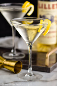 two martini glasses of Vesper Martini with lemon twist garnish and bottle of Lillet Blanc and jigger in the background