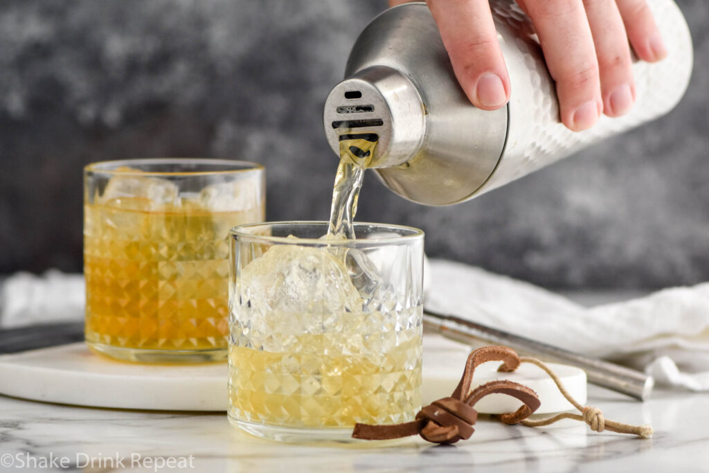 man's hand pouring shaker of whiskey sour ingredients into a glass of ice