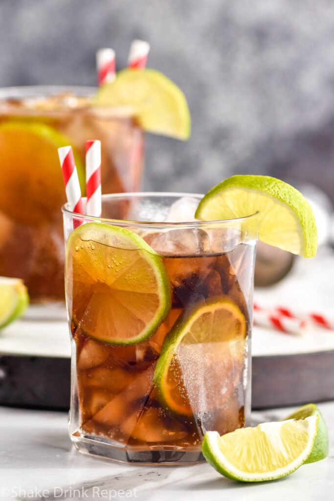 two glasses of Cuba Libre with ice, straws, and slices of lime