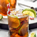 two glasses of Cuba Libre with ice, straws, and slices of lime