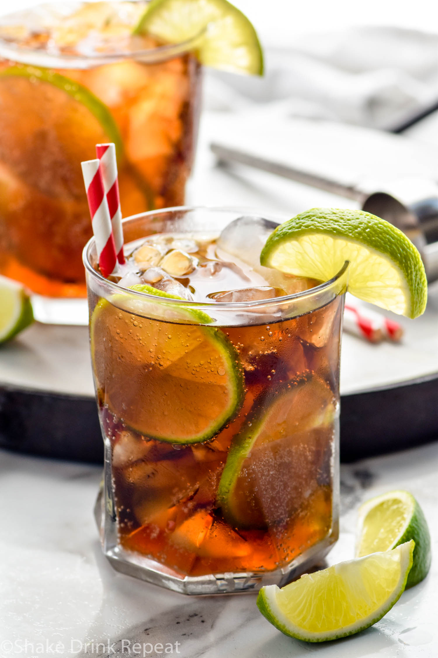 two glasses of Cuba Libre with ice, straws, and slices of lime