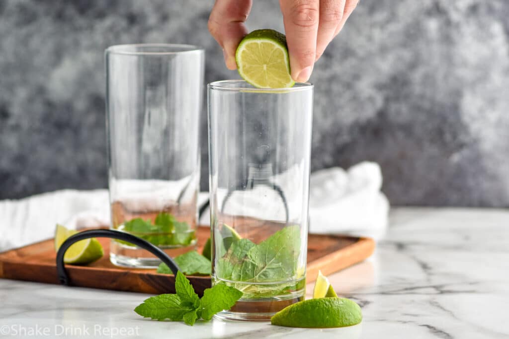 man squeezing lime into a glass with fresh mint leaves and simple syrup at the bottom to make a Mojito recipe.