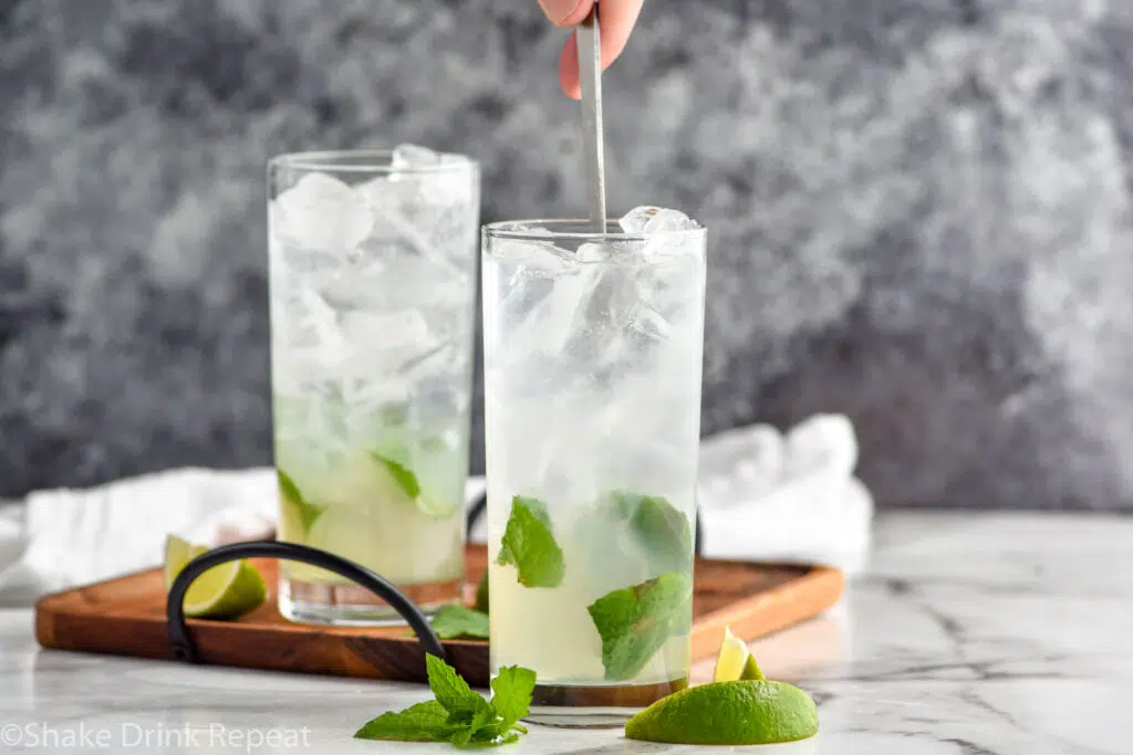 man stirring glass of Mojito recipe ingredients with ice and fresh mint leaves with a spoon
