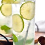 two glasses of Mojito with ice, straw, fresh mint leaves, and lime wedges
