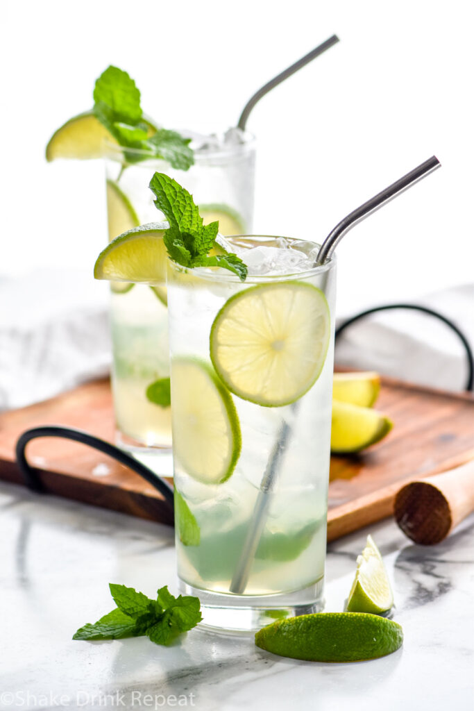 two glasses of Mojito with ice, straws, fresh mint leaves, and lime wedges