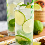 two glasses of vodka mojito with ice, slices of lime, and mint leaves with bottle of Tito's vodka in the background