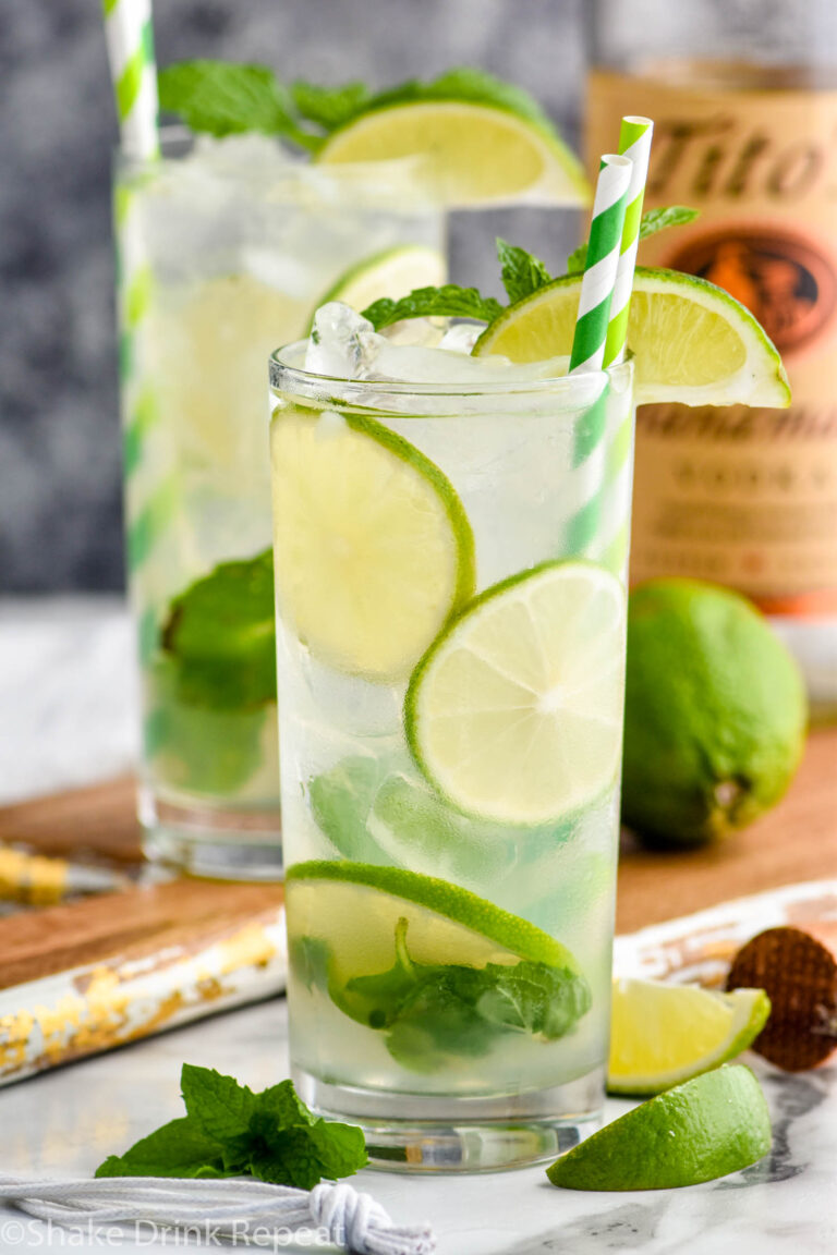 two glasses of vodka mojito with ice, slices of lime, and mint leaves with bottle of Tito's vodka in the background