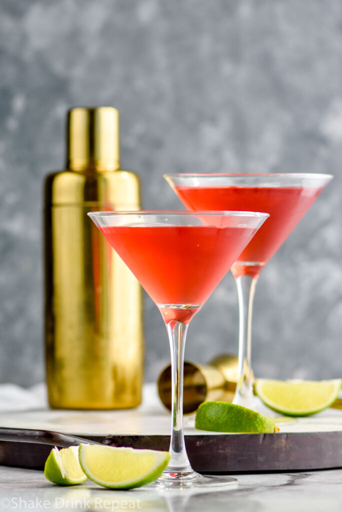 two martini glasses of Woo Woo surrounded by slices of lime and cocktail shaker