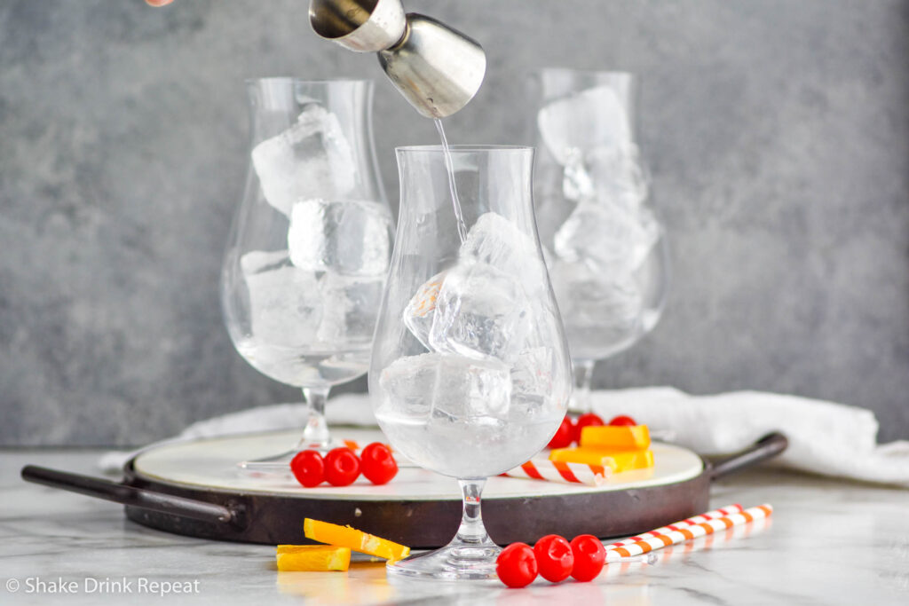 jigger of vodka pouring into a glass of ice to make a Sex on The Beach recipe surrounded by maraschino cherries and orange slices