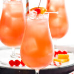 three glasses of Sex on The Beach with ice, straws, orange slices, and maraschino cherries for garnish