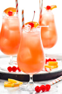 three glasses of Sex on The Beach with ice, straws, orange slices, and maraschino cherries for garnish
