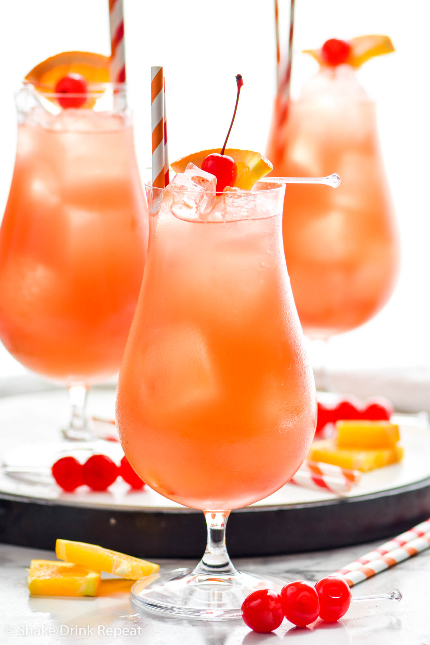 three glasses of Sex on The Beach with ice, straws, orange slices, and maraschino cherries for garnish