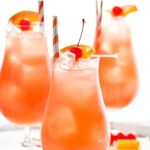 three glasses of Sex on The Beach with ice, straws, and garnished with maraschino cherries and orange slices