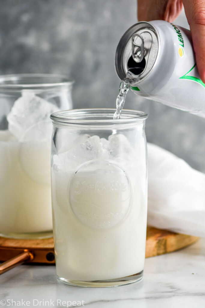 man's hand pouring can of lemon-lime soda into a glass of Drunk Ghost recipe with ice