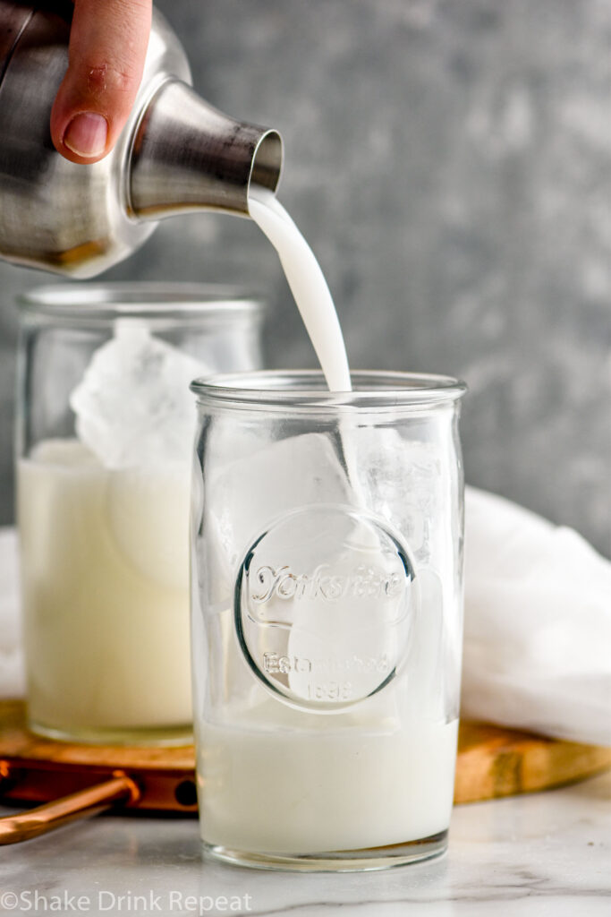 man's hand pouring shaker of Drunk Ghost ingredients into a glass of ice