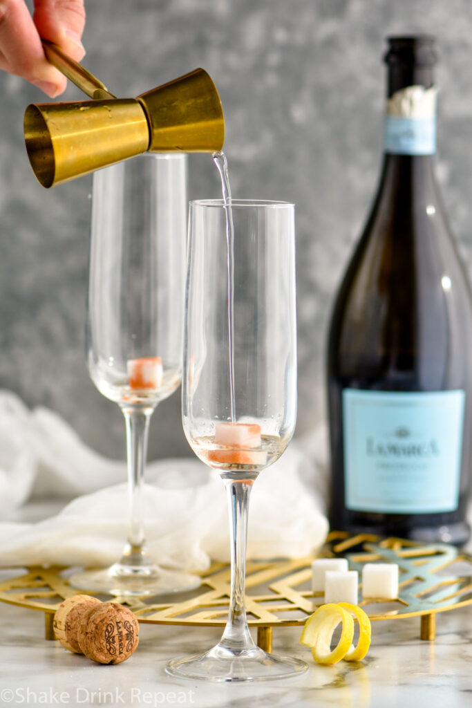 vodka being poured into a champagne flute with a sugar cube