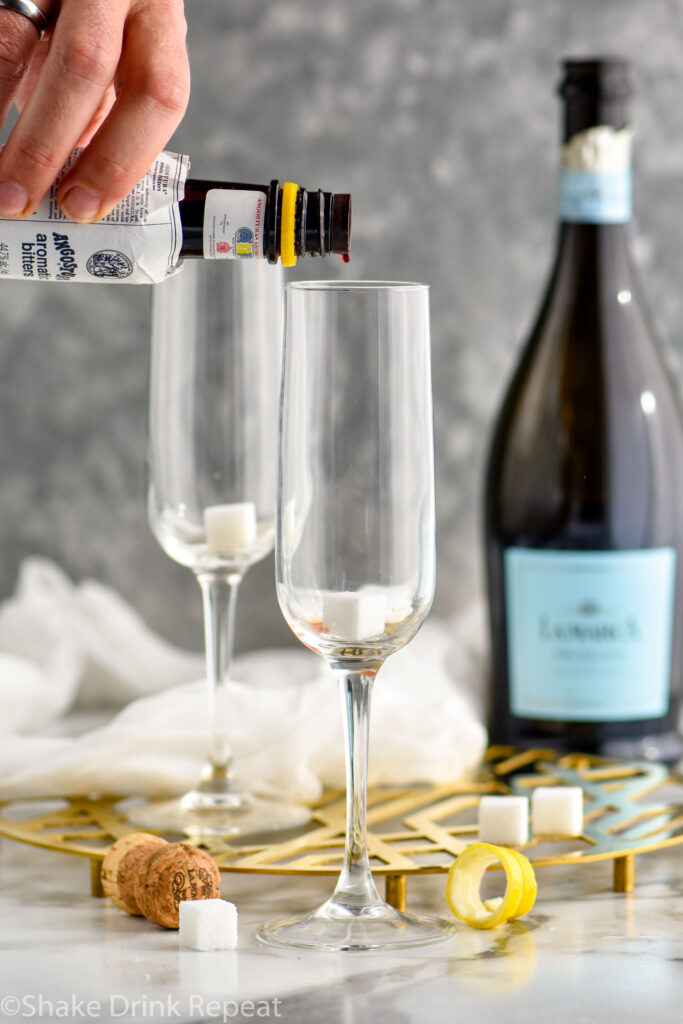 adding a few drops of bitters to a sugar cube in a champagne glass
