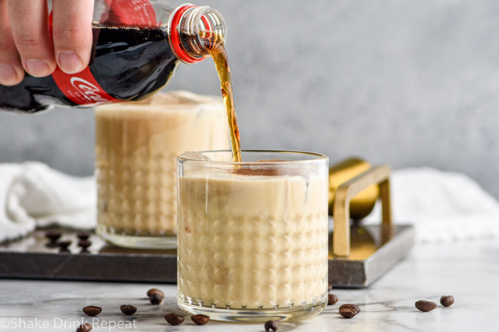 man's hand pouring bottle of cola into a glass of Colorado Bulldog recipe with ice surrounded by coffee beans