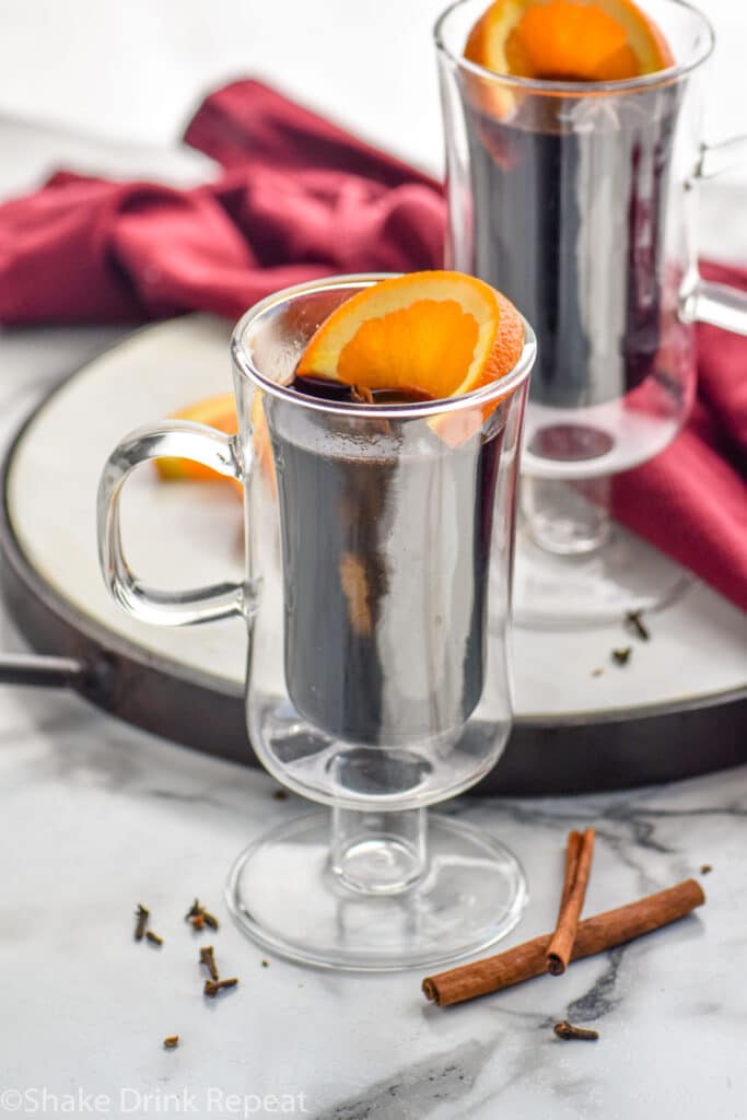 two mugs of Mulled Wine with slices of orange and clove surrounded by two cinnamon sticks
