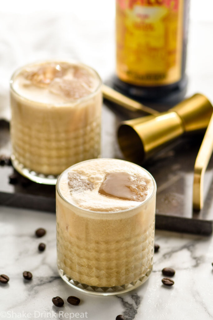 two glasses of Colorado Bulldog with ice, surrounded by coffee beans, a jigger, and bottle of Kahlua