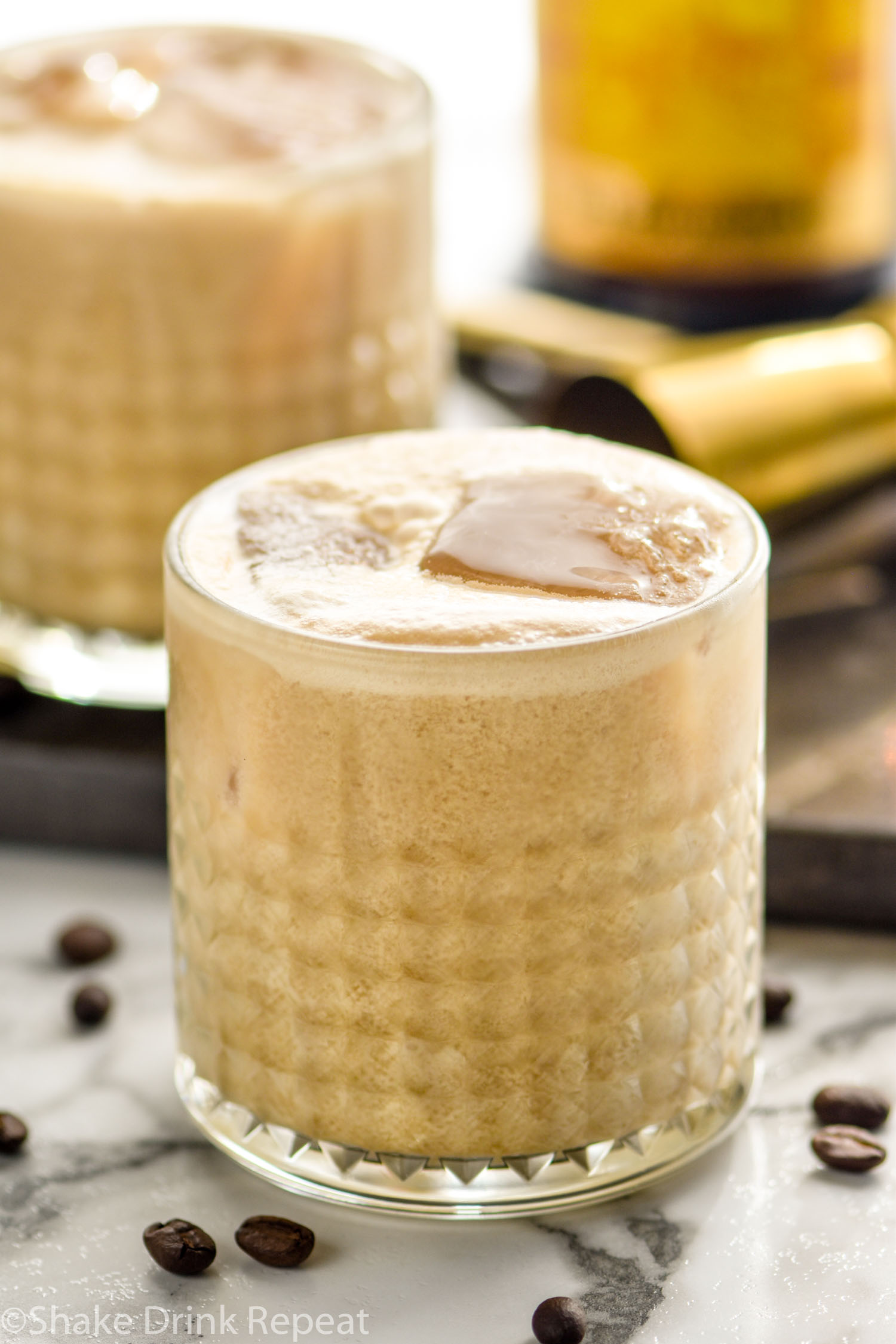 two glasses of Colorado Bulldog recipe with ice, surrounded by coffee beans and bottle of Kahlua