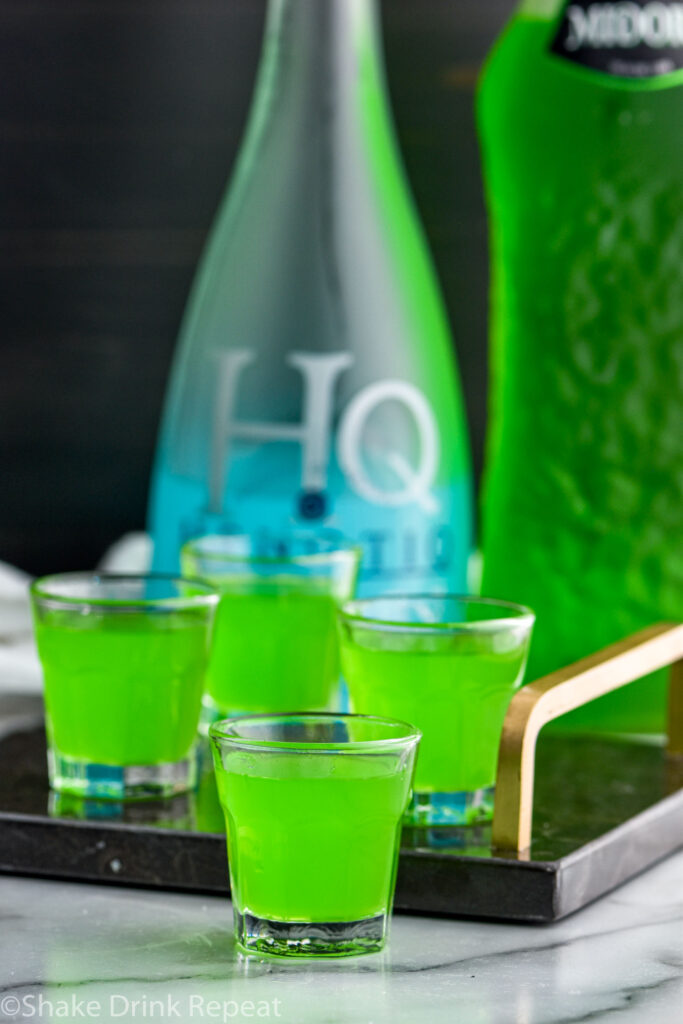 four shot glasses of Frankenstein Shot with bottles of Hpnotiq and Midori