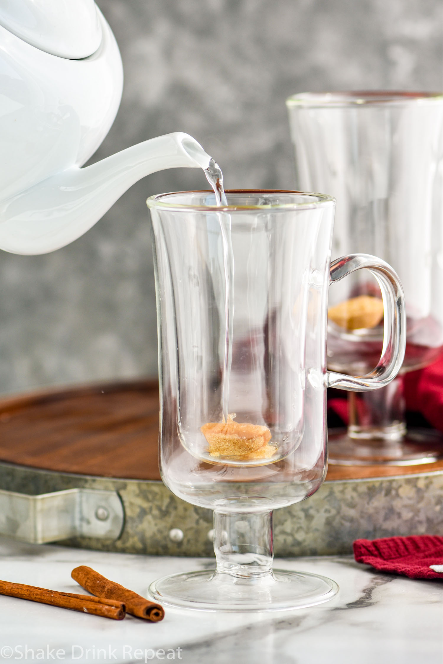 kettle of hot water pouring into a mug with brown sugar to make a Hot Buttered Rum recipe