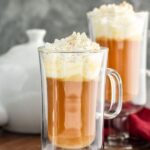 two mugs of Hot Buttered Rum recipe topped with whipped cream and nutmeg and surrounded by cinnamon sticks