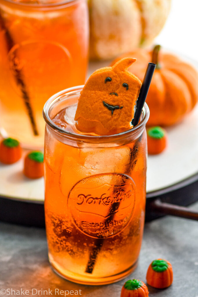 two glasses of drunk pumpkin cocktail recipe with ice, straws, and garnished with pumpkin candies