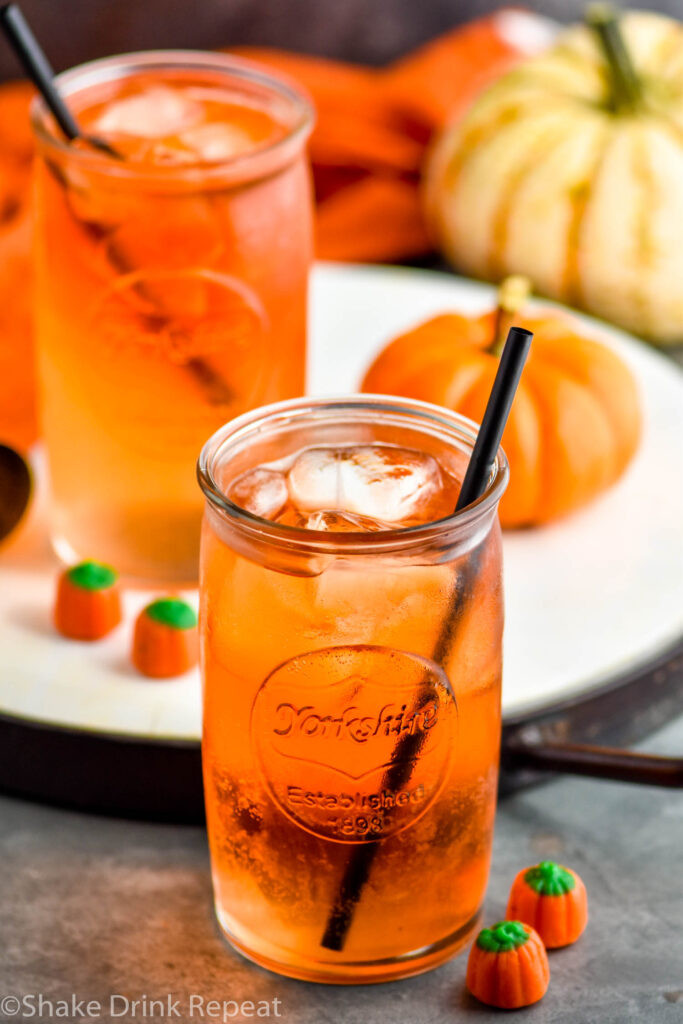 two glasses of Drunk Pumpkin cocktail with ice and straws and surrounded by pumpkin candy