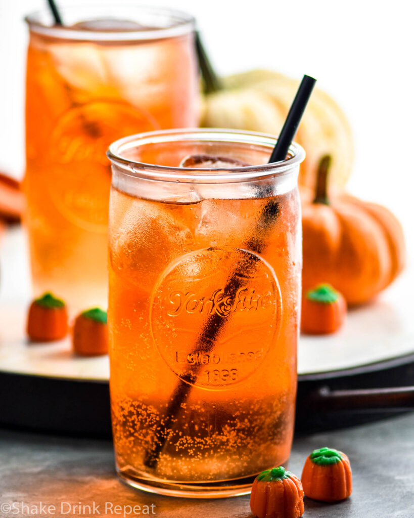 two glasses of Drunk Pumpkin cocktail recipe with ice, straw, and surrounded by pumpkin candy