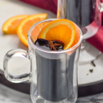 two mugs of mulled wine with orange slice, clove, and two cinnamon sticks