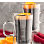 two mugs of Mulled Wine with orange slices and cinnamon sticks