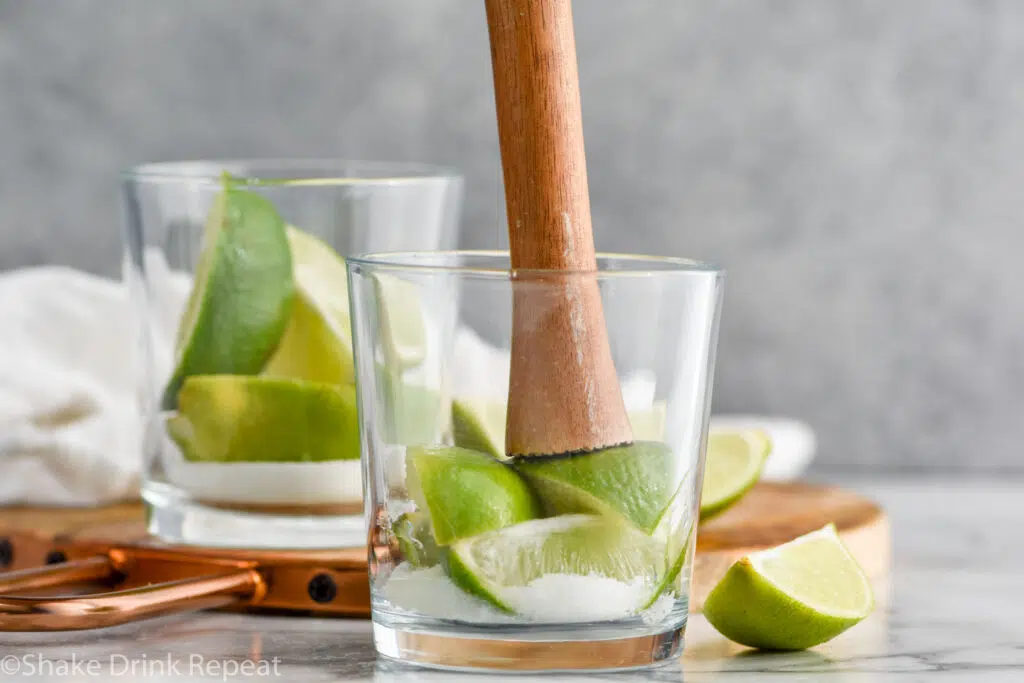 muddling fresh limes with sugar in a glass to make a Caipirinha recipe