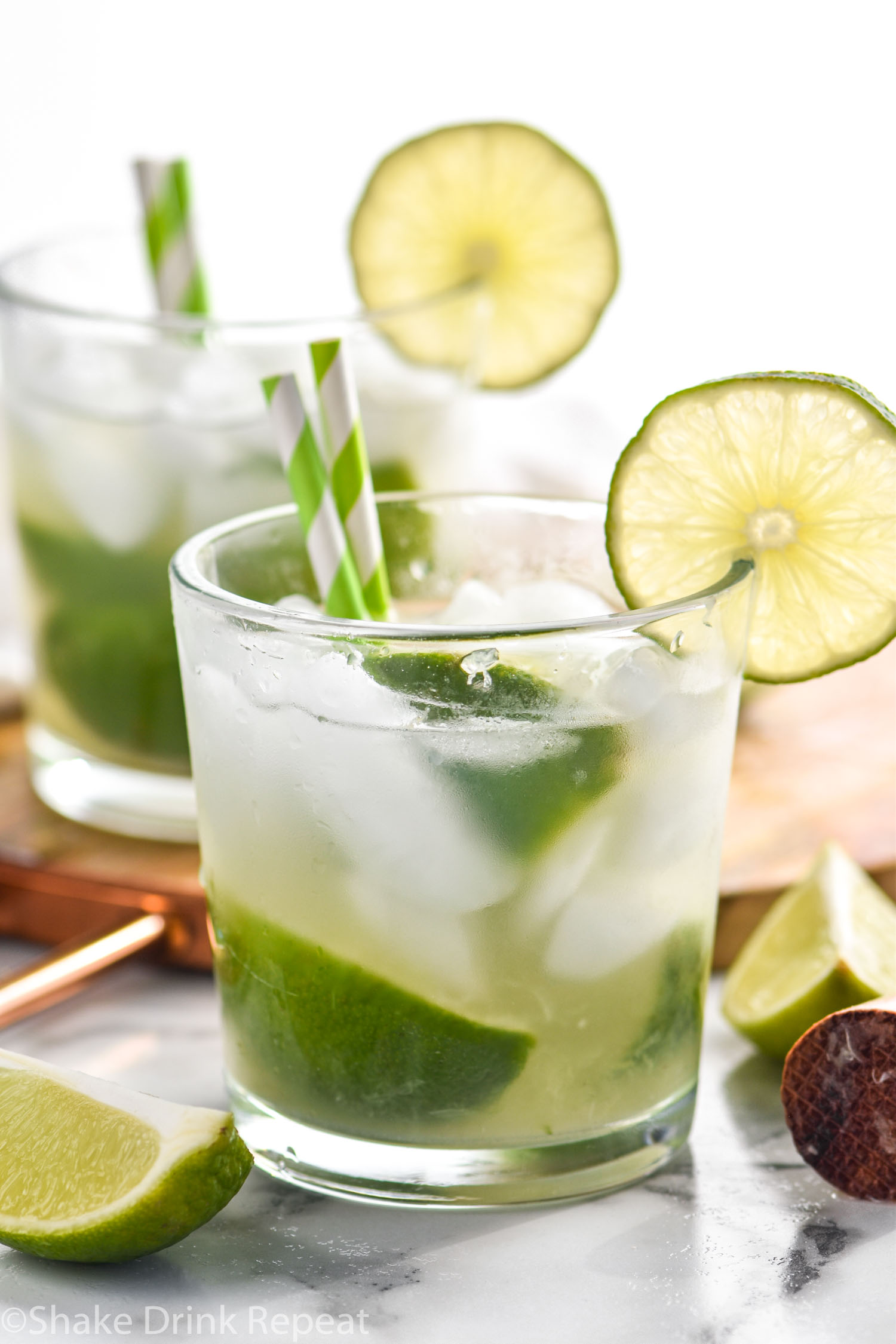 two glasses of Caipirinha recipe with ice, limes, and straws