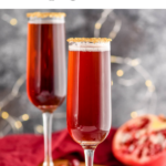 two glasses of Cranberry Pomegranate Champagne Cocktail recipe rimmed with gold sprinkles surrounded by pomegranate seeds and cranberries