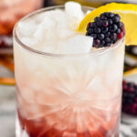glass of Bramble recipe with ice, garnished with fresh blackberries and a slice of lemon