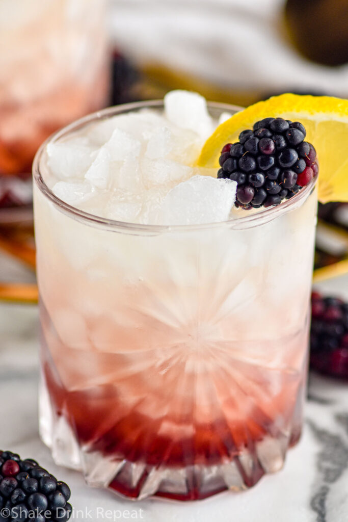 glass of Bramble recipe with ice, garnished with fresh blackberries and a slice of lemon