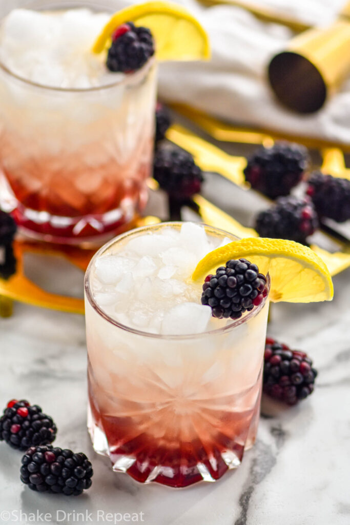 two glasses of Bramble recipe with ice garnished with fresh blackberries and slices of lemon