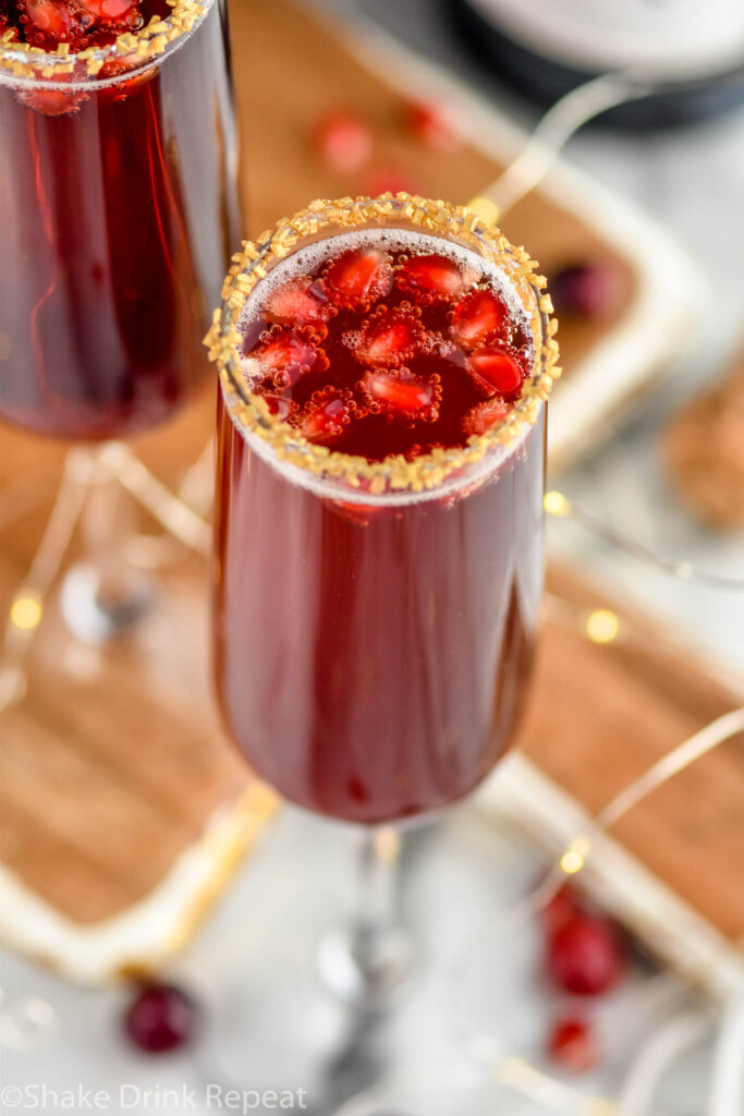 two glasses of Cranberry Pomegranate Champagne Cocktail garnished with gold sprinkles and pomegranate seeds