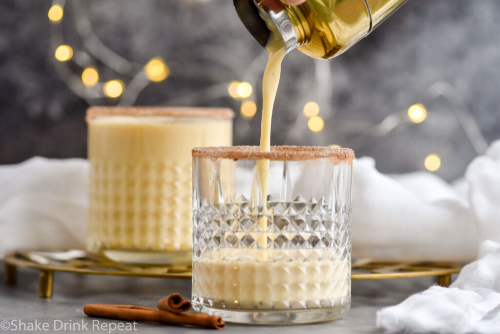 cocktail shaker of Fireball Eggnog ingredients pouring into a glass with cinnamon sugar rim