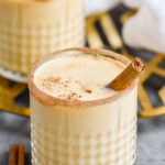 two glasses of Fireball Eggnog recipe garnished with cinnamon sugar rim, cinnamon sticks, and nutmeg