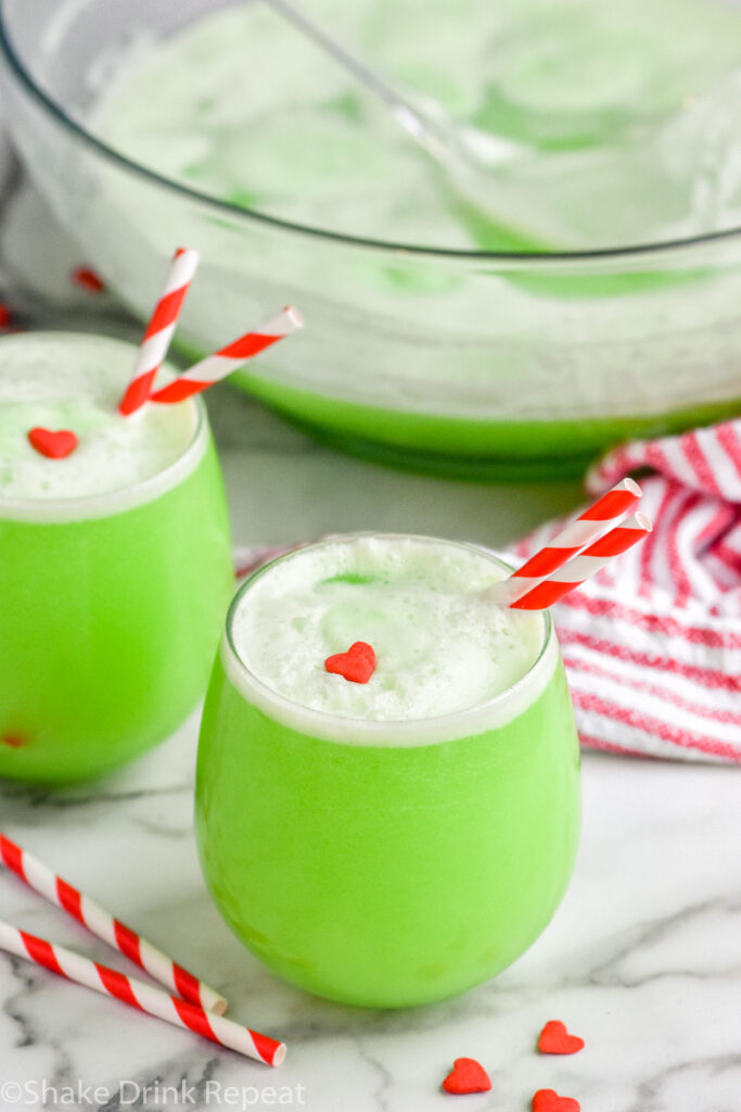 two glasses and a punch bowl of Grinch Punch with straws and candy heart garnish