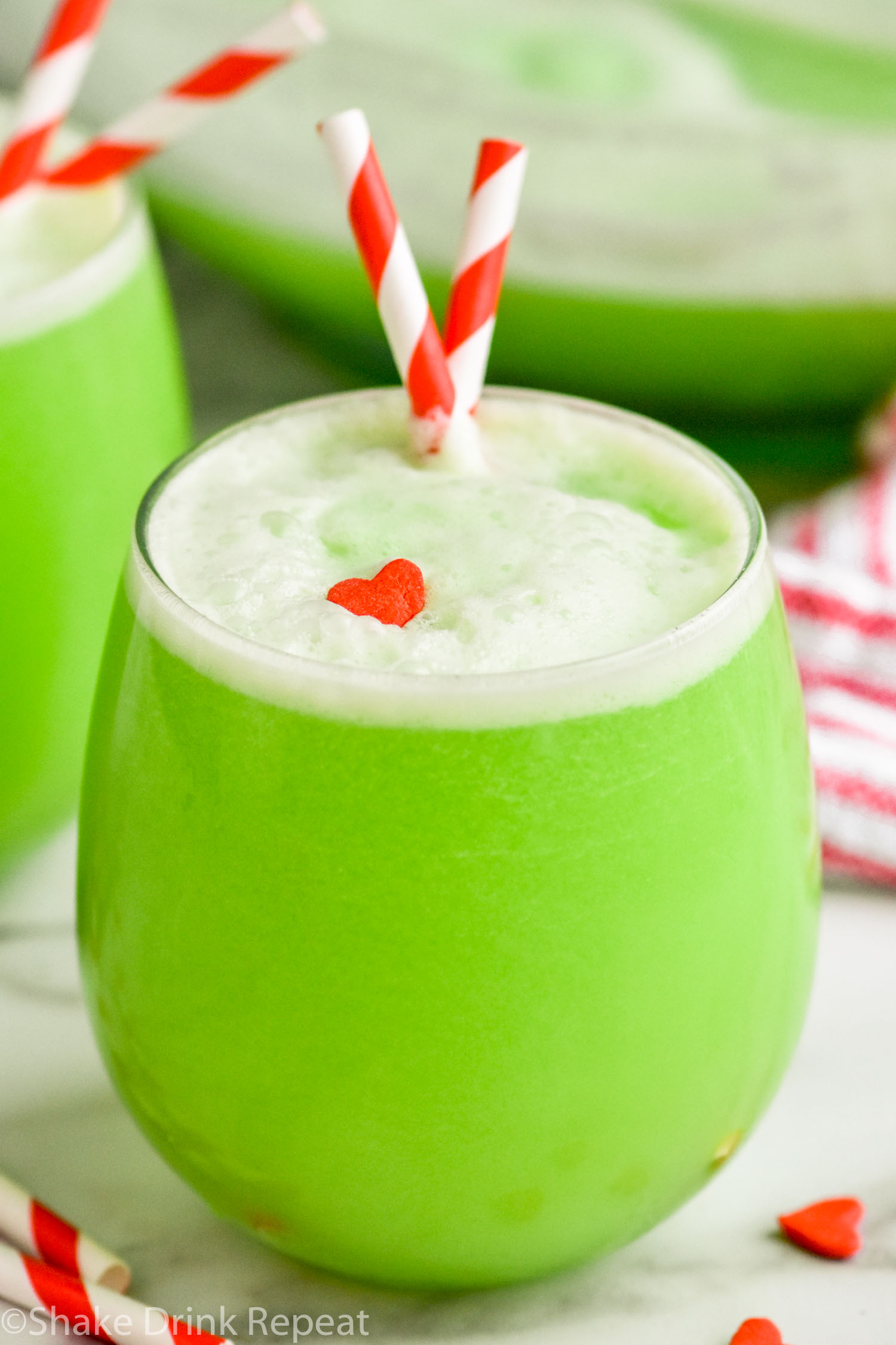 glass of Grinch Punch recipe with straws and a candy heart