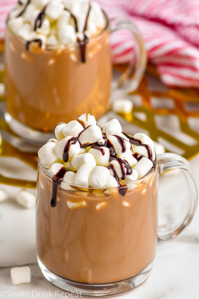 two mugs of Spiked Hot Chocolate recipe topped with marshmallows and chocolate drizzle