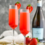 two champagne flutes of Rossini recipe garnished with a strawberry with bottle of Prosecco in the background