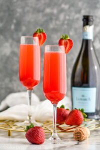 two champagne flutes of Rossini recipe garnished with a strawberry with bottle of Prosecco in the background