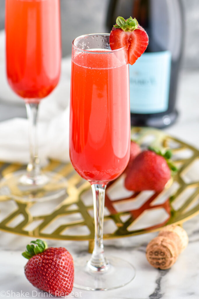 two champagne flutes of Rossini recipe garnished with a strawberry with bottle of Prosecco in the background