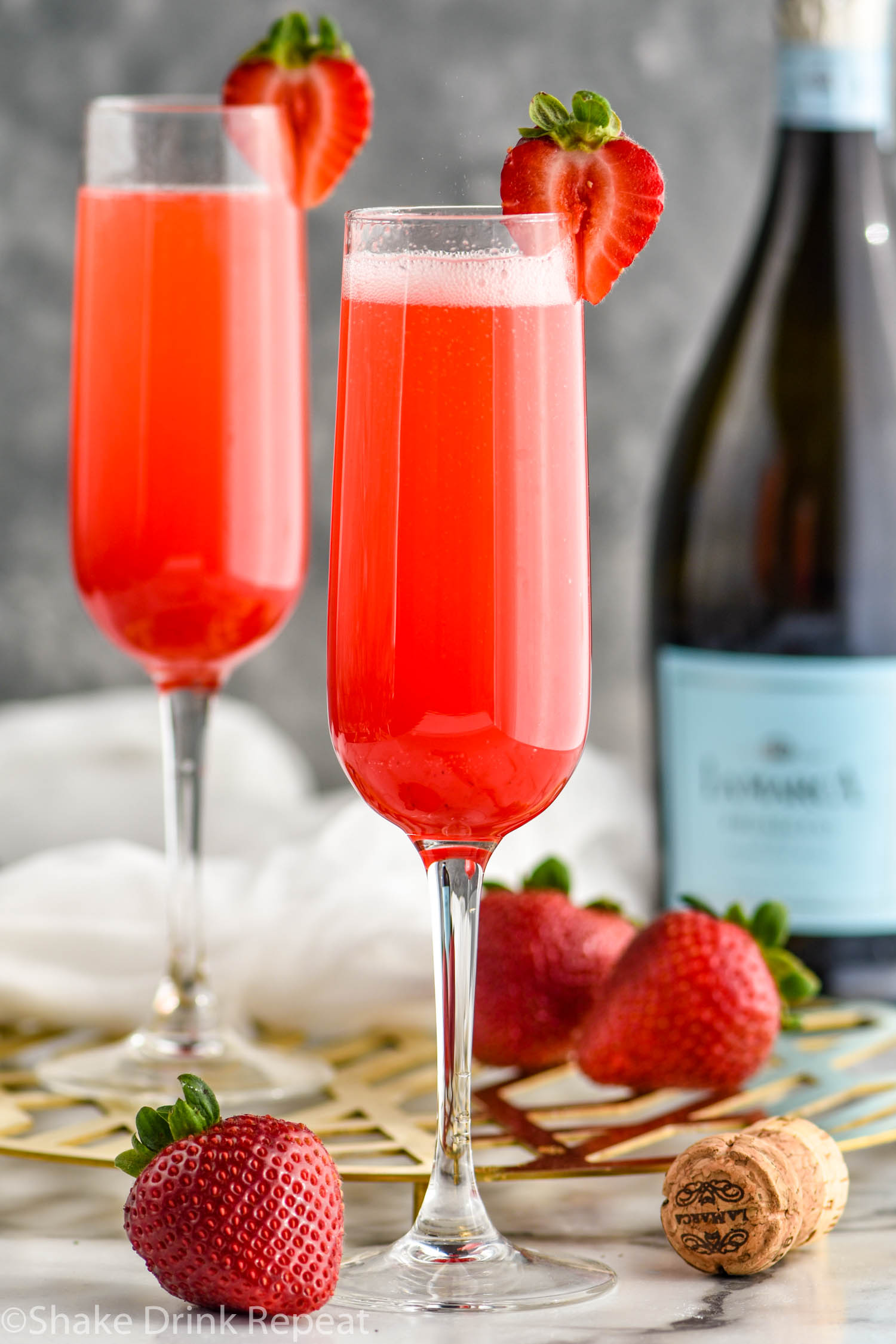 two champagne flutes of Rossini recipe garnished with a strawberry with bottle of Prosecco in the background