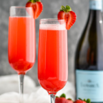 two champagne flutes of Rossini recipe garnished with a strawberry with bottle of Prosecco in the background